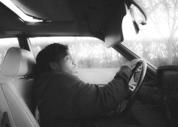 a man sitting in a car with his hand on the steering wheel