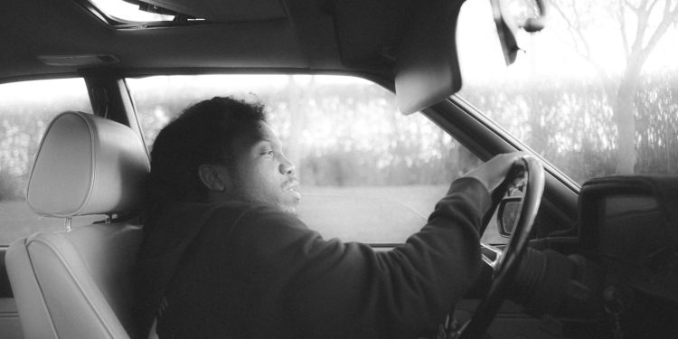 a man sitting in a car with his hand on the steering wheel